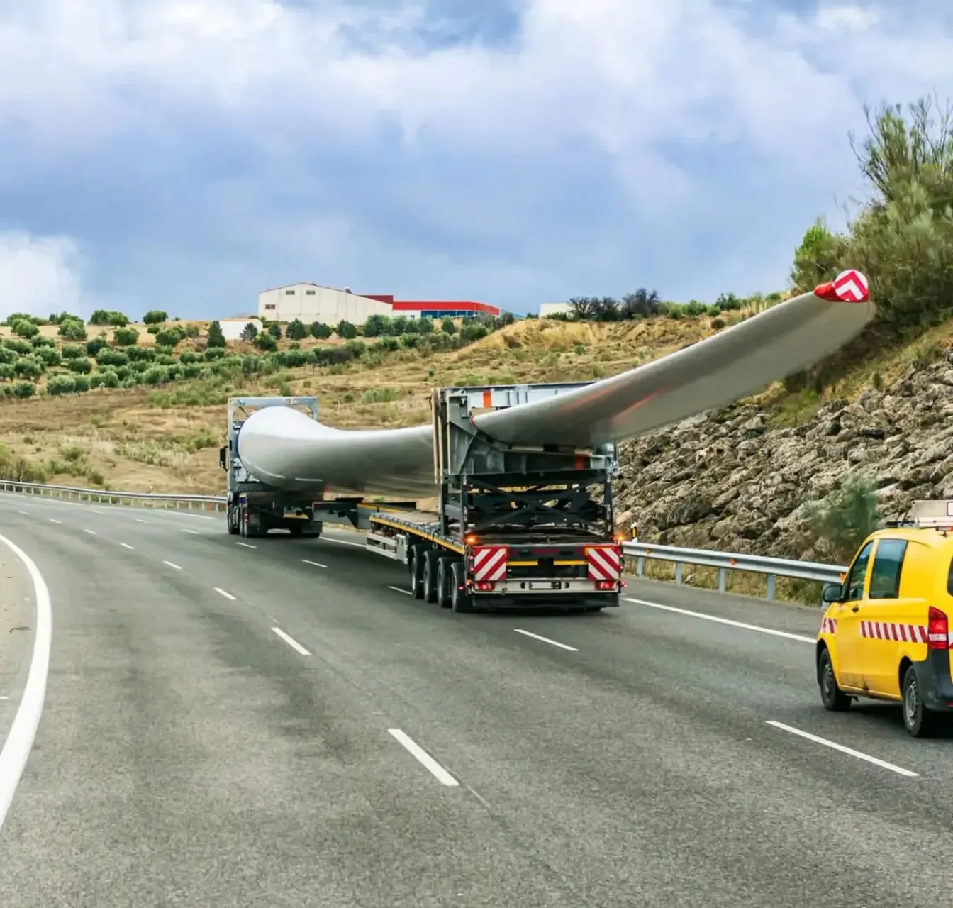 Wind turbine blades on extendable trailers, travelling in convoy with an escort vehicle